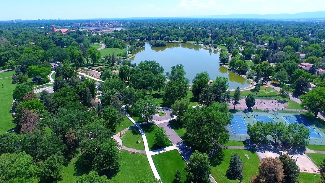 A large green park with a lake and tennis courts.